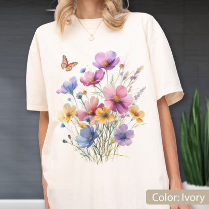 May include: An ivory short-sleeve t-shirt featuring a colorful graphic print of a wildflower bouquet with pink, yellow, and blue blossoms, green stems, and a single orange butterfly. The shirt has a crew neckline and a relaxed, loose fit.