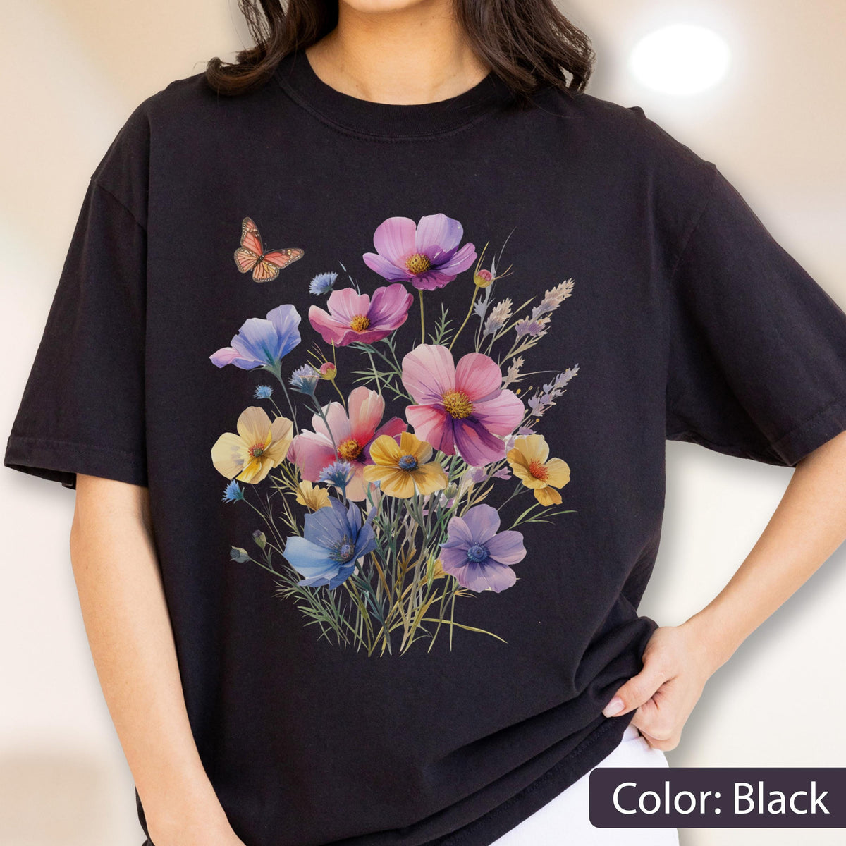 May include: A black short-sleeved t-shirt featuring a central graphic print of a colorful wildflower bouquet in shades of pink, purple, blue, and yellow, accompanied by a small orange butterfly positioned to the upper left of the floral arrangement.