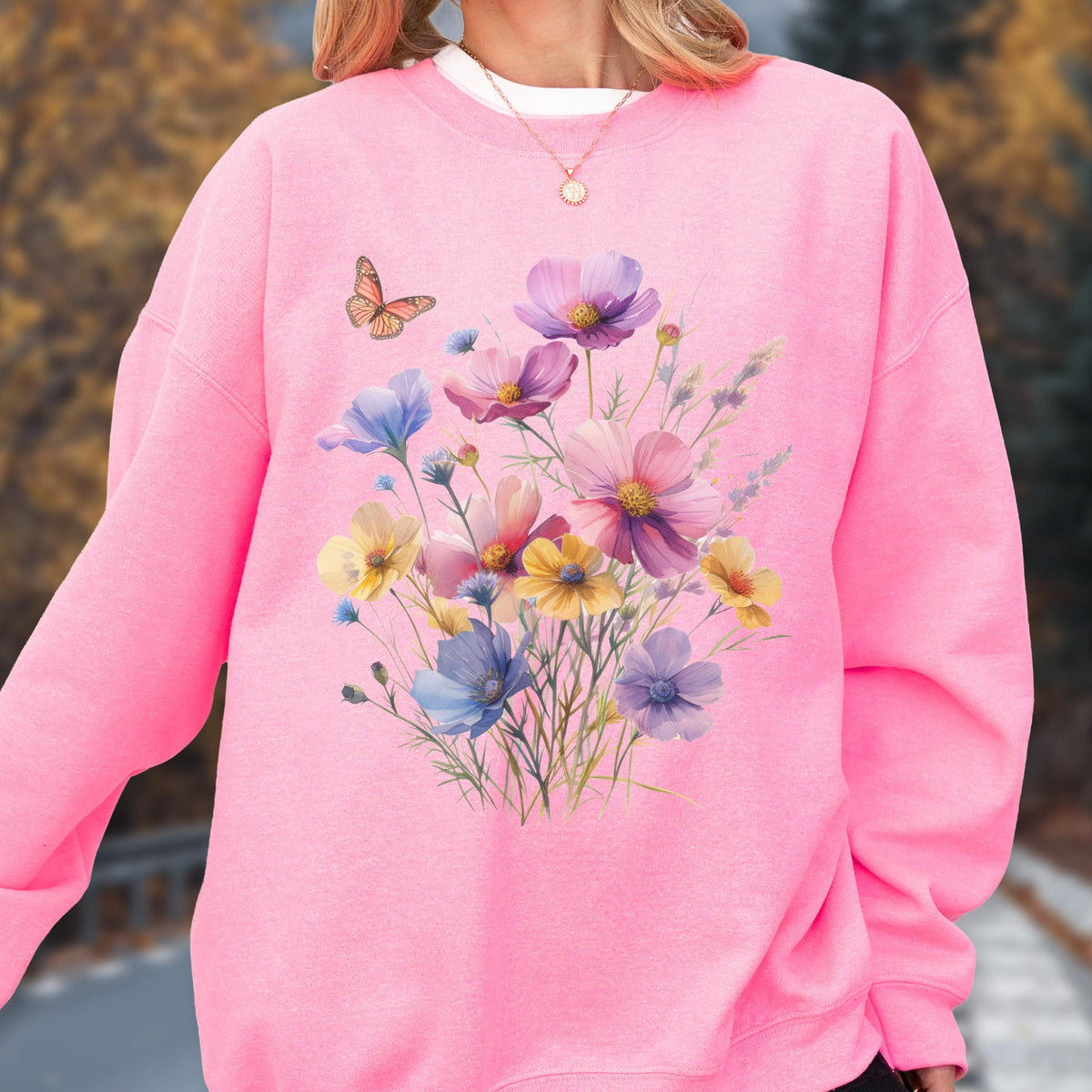 May include: A pink sweatshirt featuring a watercolor floral design with a butterfly. The floral arrangement includes purple, pink, yellow, and blue flowers. The sweatshirt has a crew neck and long sleeves.