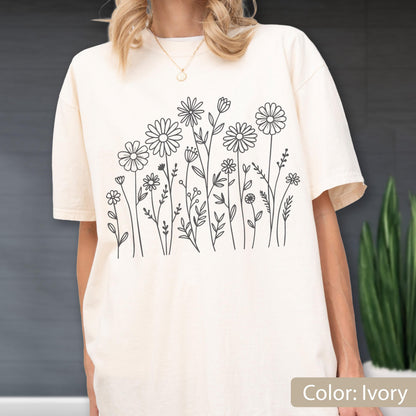 May include: An ivory t-shirt featuring a black line art graphic of various wildflowers and daisies across the front. The shirt has a crew neckline and short sleeves, showcasing a simple botanical illustration of stems, leaves, and flower heads.