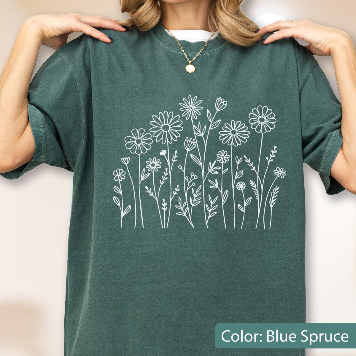 May include: A blue spruce short-sleeve t-shirt featuring a white line art graphic of various wildflowers and stems across the chest. The shirt has a crew neckline and a relaxed fit, showcasing a simple botanical illustration in white ink.