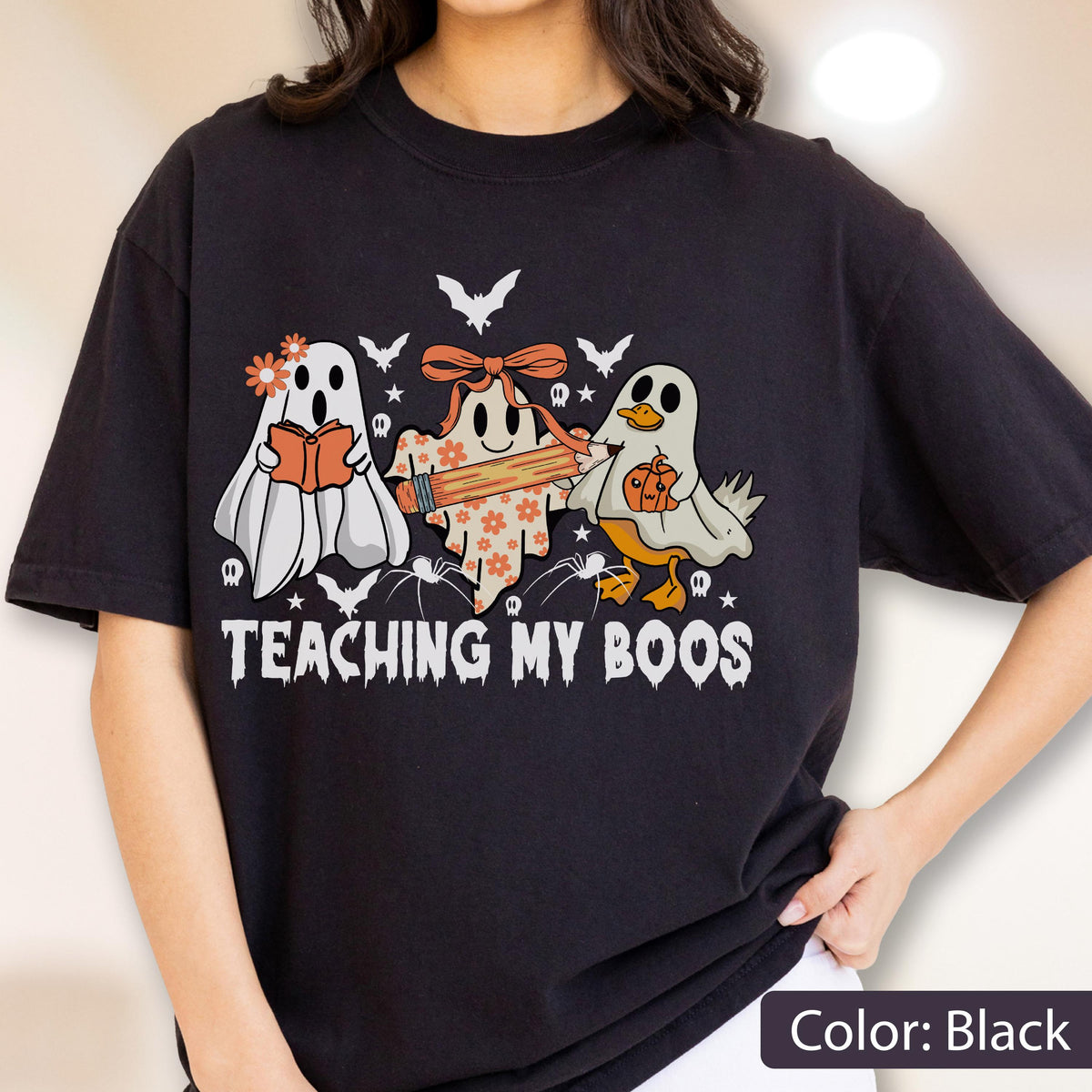 May include: Black t-shirt with a Halloween-themed graphic. The design features three cartoon ghosts, one reading a book, one holding a pencil, and one with a pumpkin. The text "TEACHING MY BOOS" is below the ghosts.