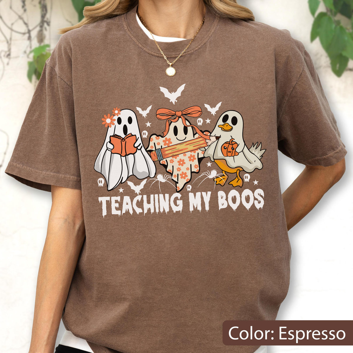 May include: Espresso-colored t-shirt featuring a Halloween-themed graphic. The design includes three cartoon ghosts, each with unique accessories, and the text "TEACHING MY BOOS". Bats and spiders are also included in the design.