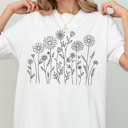 May include: A white short-sleeved t-shirt featuring a black line art graphic of various wildflowers and stems across the center. The design includes multiple daisy-like flowers, small buds, and leafy sprigs arranged in a botanical illustration style.