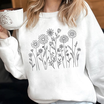 May include: A white crewneck sweatshirt featuring a black line art illustration of various wildflowers and daisies centered on the chest. The design consists of multiple stems, leaves, and flower heads arranged in a botanical pattern on the fabric.