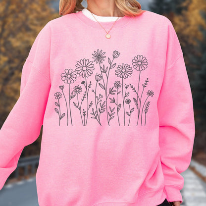 May include: A bright pink crewneck sweatshirt featuring a black line art illustration of various wildflowers and daisies across the chest. The garment has long sleeves, a ribbed neckline, and a simple, clean design with no additional text or patterns.