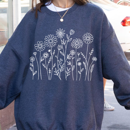 May include: A dark heather navy blue crewneck sweatshirt featuring a white line art graphic of various wildflowers and stems across the chest. The long-sleeved garment has a ribbed collar, cuffs, and hem, showcasing a simple botanical illustration.