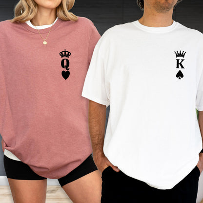 May include: A pair of matching shirts, one dusty rose and one white. The dusty rose shirt features a black crown, the letter "Q", and a heart. The white shirt has a black crown, the letter "K", and a spade. The shirts are casual wear.