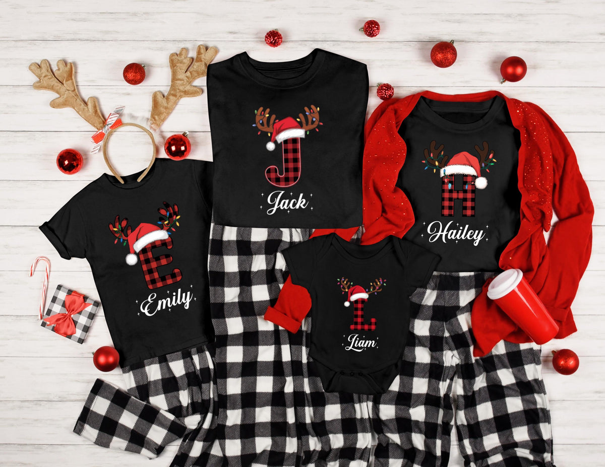 May include: Black family Christmas pajamas with reindeer antlers, Santa hats, and names. The shirts have the letters E, J, H, and L in a red and black plaid pattern. The pajamas are black and white checkered.