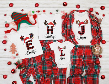 May include: Matching family Christmas pajamas in red and green plaid. White shirts with reindeer antlers, Santa hats, and initial letters. The names "Emily", "Hailey", "Jack", and "Liam" are printed below the letters. A Christmas hat and ornaments complete the festive scene.