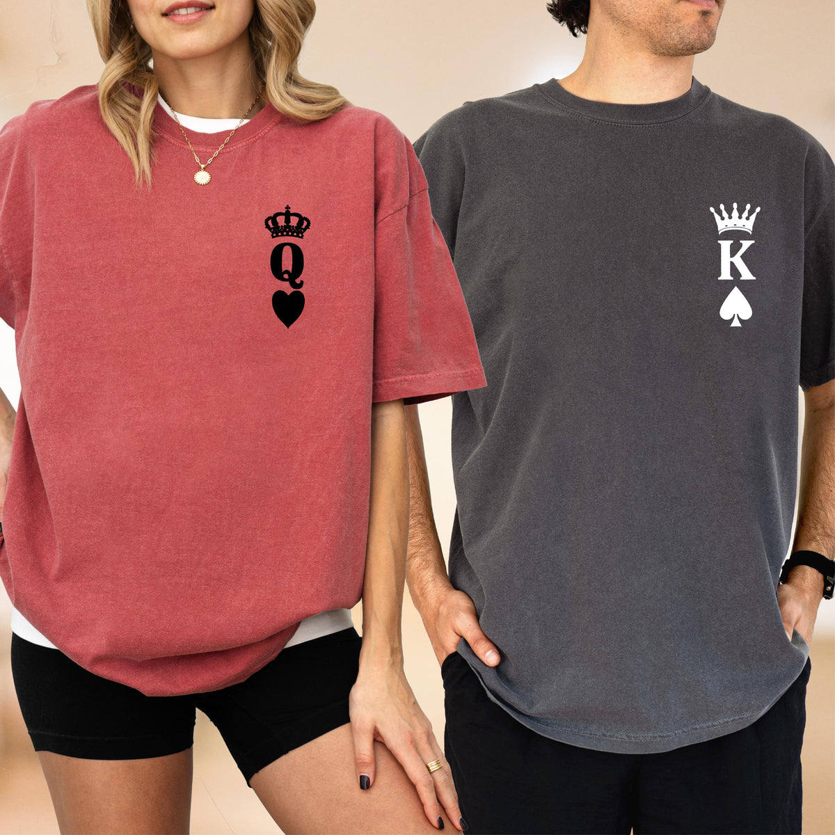 May include: A red t-shirt with a black graphic of a crown above the letter Q and a heart symbol on the chest, paired with a charcoal gray t-shirt featuring a white graphic of a crown above the letter K and a spade symbol on the chest.