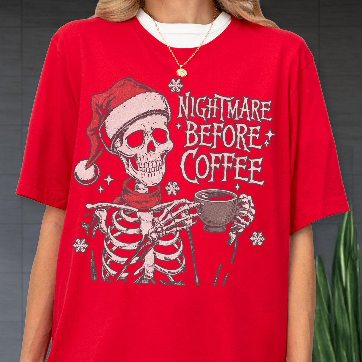 May include: Red t-shirt featuring a skeleton wearing a Santa hat and scarf, holding a coffee cup. The text "NIGHTMARE BEFORE COFFEE" is printed on the shirt, along with snowflake graphics. The shirt has a white collar.