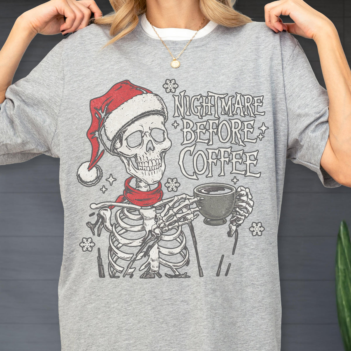May include: A gray t-shirt featuring a skeleton wearing a Santa hat and a red scarf, holding a coffee cup. The text "NIGHTMARE BEFORE COFFEE" is printed above the skeleton.