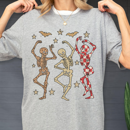 May include: A gray sweatshirt featuring a graphic of three dancing skeletons in various colors. The skeletons are surrounded by stars and bats. The sweatshirt has a white collar and is being held up by a person.