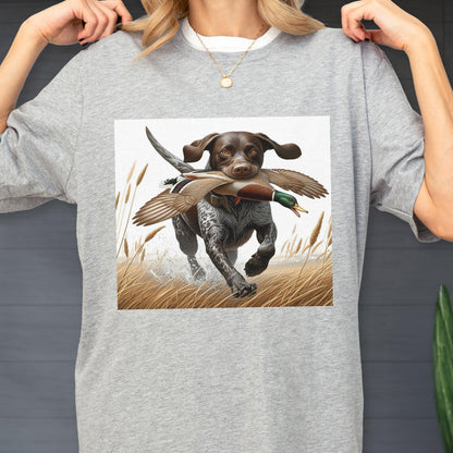 May include: Gray crew neck t-shirt featuring a graphic of a brown and white dog running through tall grass, carrying a duck in its mouth. The dog is in mid-stride, with water splashing around its paws. The duck has brown and green feathers.