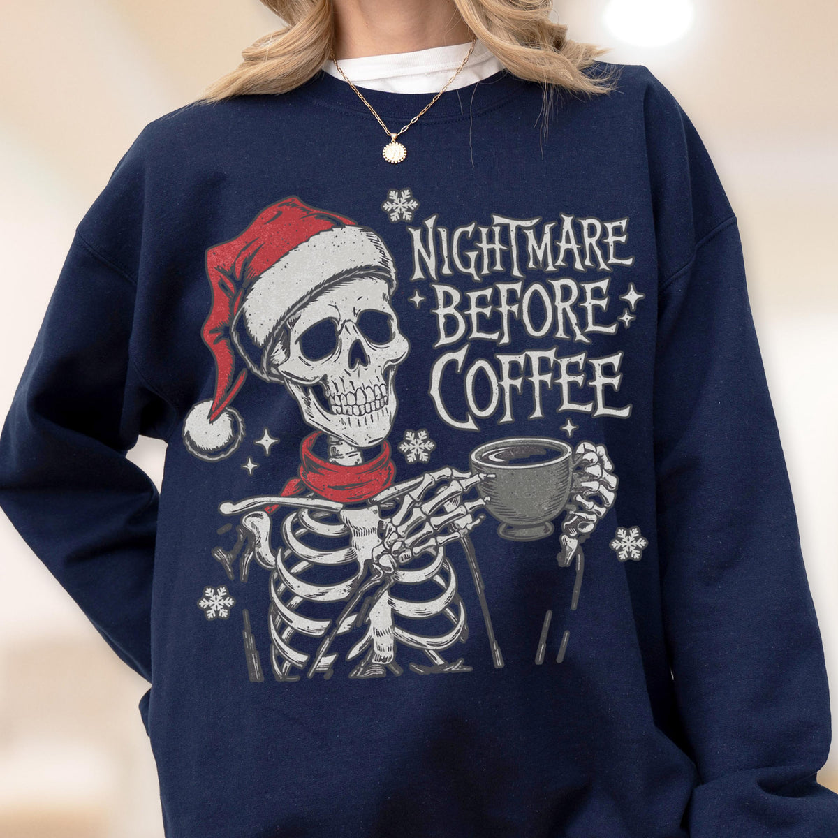 May include: Navy blue sweatshirt featuring a skeleton wearing a Santa hat and red scarf, holding a coffee cup. The text "NIGHTMARE BEFORE COFFEE" is printed on the front, with snowflake accents. A festive and spooky design.