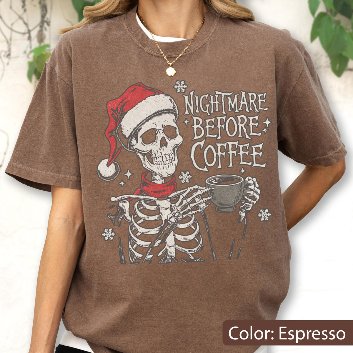 May include: Espresso-colored t-shirt featuring a skeleton wearing a Santa hat and scarf, holding a coffee cup. The text "NIGHTMARE BEFORE COFFEE" is printed on the shirt, along with snowflake graphics. A casual, festive design.