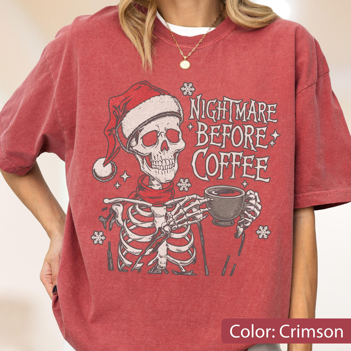 May include: Crimson-colored t-shirt featuring a skeleton wearing a Santa hat and scarf, holding a coffee cup. The text "Nightmare Before Coffee" is printed on the shirt, along with snowflake and star graphics. A festive and spooky design.