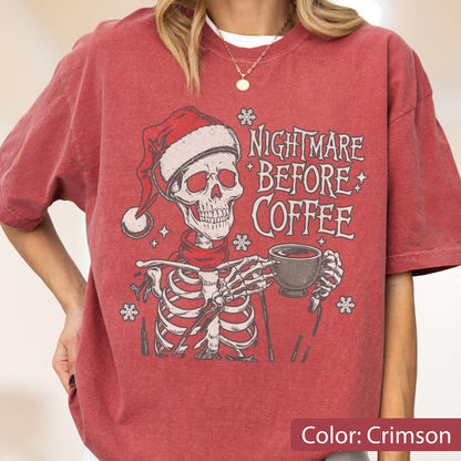 May include: Crimson-colored t-shirt featuring a skeleton wearing a Santa hat and scarf, holding a coffee cup. The text "Nightmare Before Coffee" is printed on the shirt, along with snowflake and star graphics. A festive and spooky design.