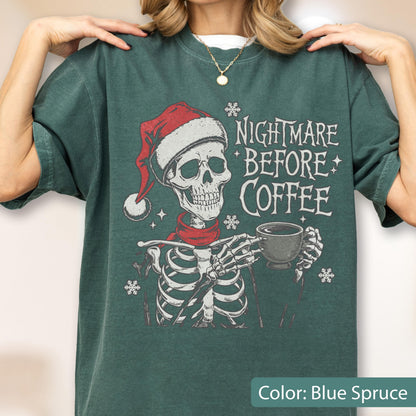 May include: Blue spruce-colored t-shirt featuring a skeleton wearing a Santa hat and red scarf, holding a coffee cup. The text "NIGHTMARE BEFORE COFFEE" is printed above the skeleton. Snowflake graphics are also included.