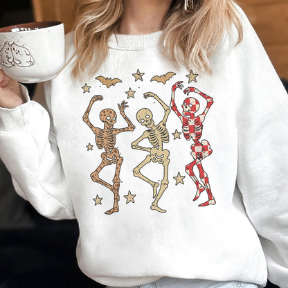 May include: White sweatshirt featuring a graphic of three dancing skeletons in brown, beige, and red. The design includes bats and stars, creating a festive Halloween theme. The sweatshirt is a comfortable, casual style.