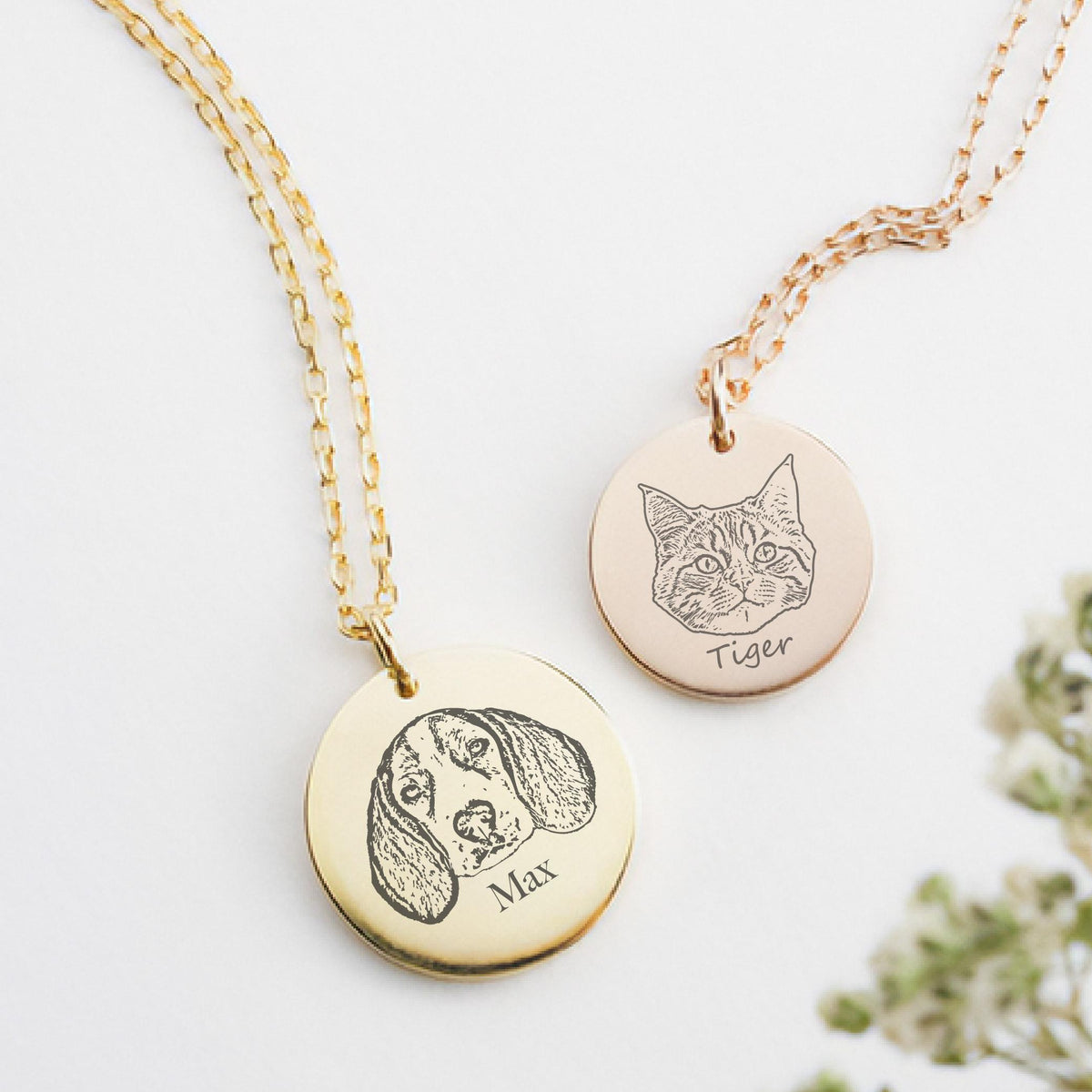 May include: Two gold-colored pendant necklaces. One pendant features a dog portrait with the name "Max" engraved below. The other pendant has a cat portrait with the name "Tiger". Both pendants hang from delicate gold chains.