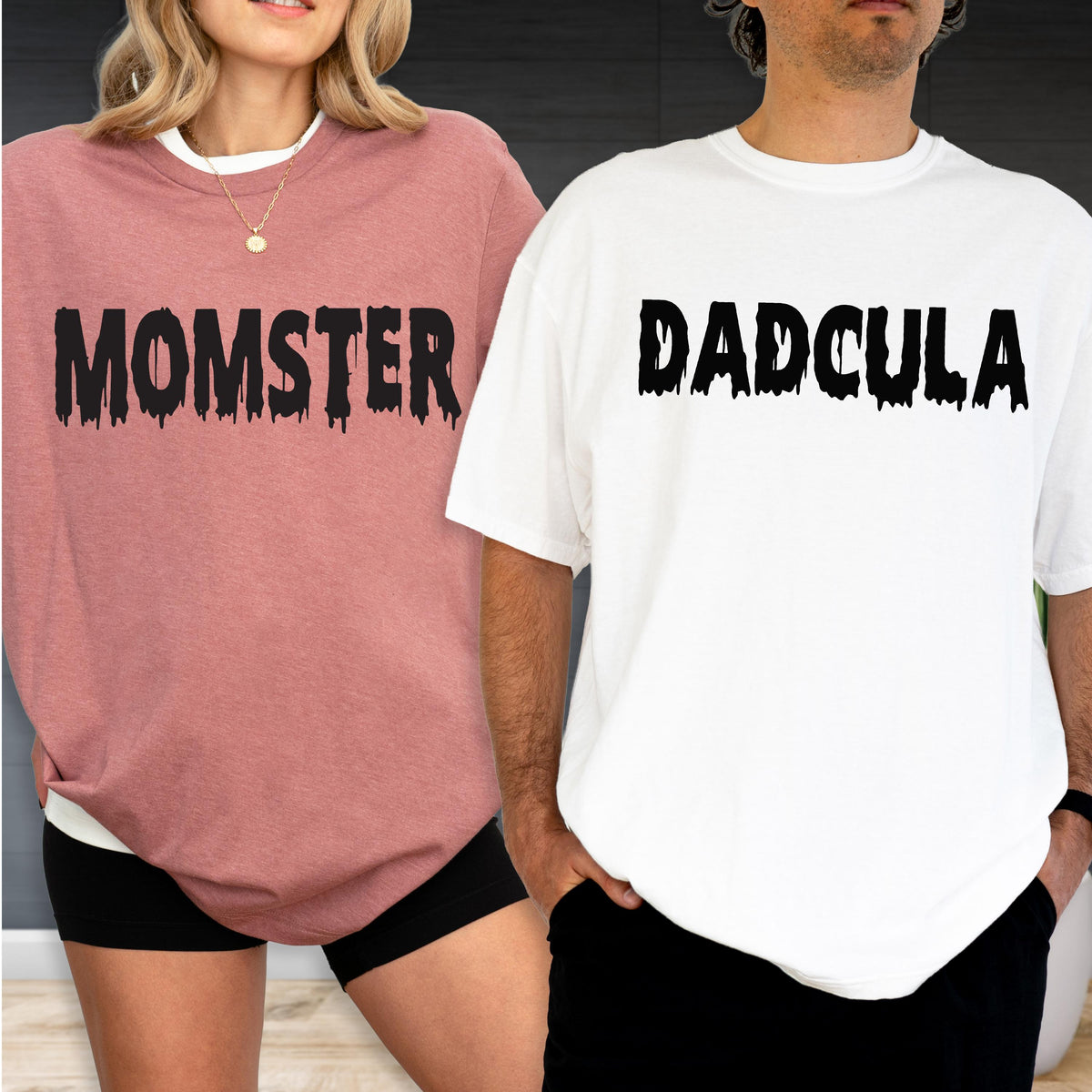 May include: A dusty rose t-shirt with the black text MOMSTER in a dripping font and a white t-shirt with the black text DADCULA in a dripping font. Both shirts feature short sleeves, crew necklines, and a relaxed fit for casual wear.