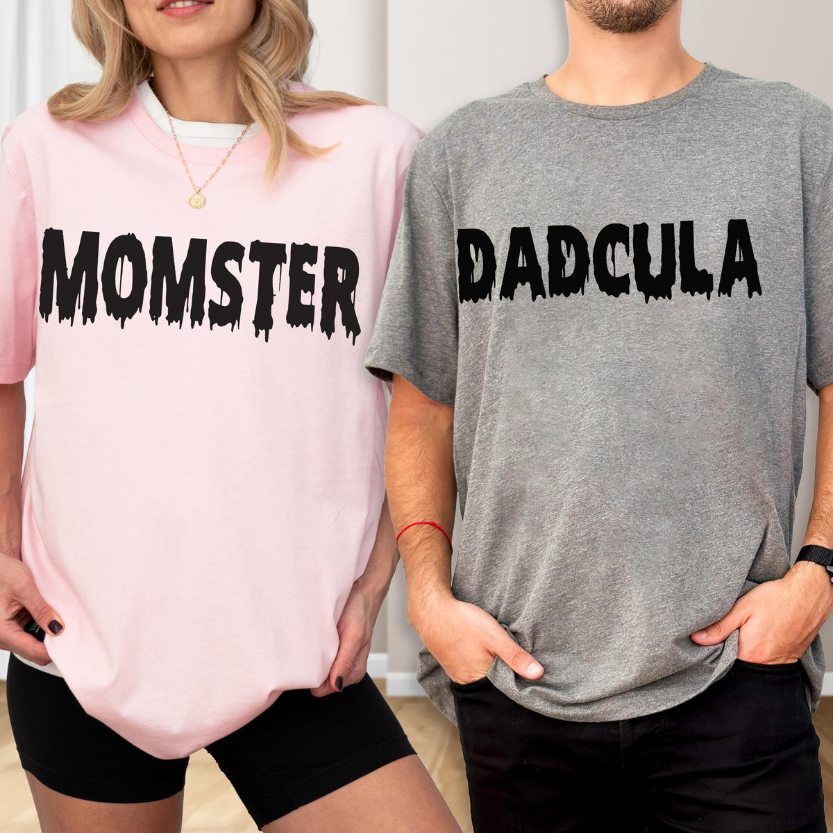 May include: A light pink t-shirt with the black text MOMSTER in a dripping font and a heather gray t-shirt with the black text DADCULA in a dripping font. Both shirts feature short sleeves and a crew neckline, presented as a matching set.