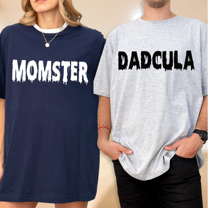 May include: A navy blue t-shirt with the white text MOMSTER in a dripping font and a light gray t-shirt with the black text DADCULA in a dripping font. Both shirts feature short sleeves and a crew neckline, displaying a graphic design.