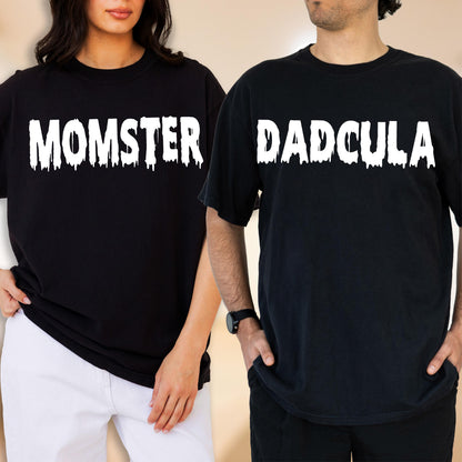 May include: Two black short-sleeved t-shirts. The left shirt features the white text MOMSTER in a dripping font style. The right shirt features the white text DADCULA in a matching dripping font style. Both shirts have a crew neckline.