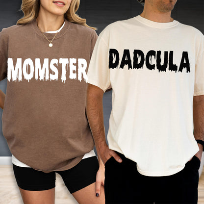 May include: A brown t-shirt with the white text MOMSTER in a dripping font and a cream t-shirt with the black text DADCULA in a dripping font. Both shirts feature a crew neckline and short sleeves, showcasing a graphic design on the chest.