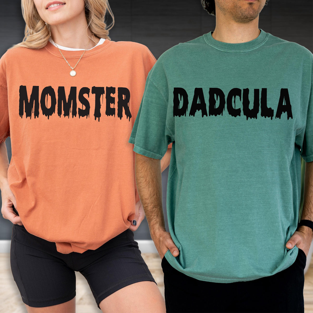 May include: An orange t-shirt with the black text MOMSTER in a dripping font and a green t-shirt with the black text DADCULA in a dripping font. Both shirts feature short sleeves and a crew neckline, showcasing a casual and relaxed fit.