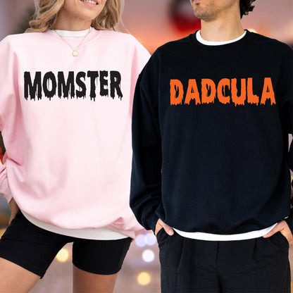 May include: Pink sweatshirt with the word "MOMSTER" in black dripping font. A black sweatshirt with the word "DADCULA" in orange dripping font. The sweatshirts are part of a Halloween-themed matching set.