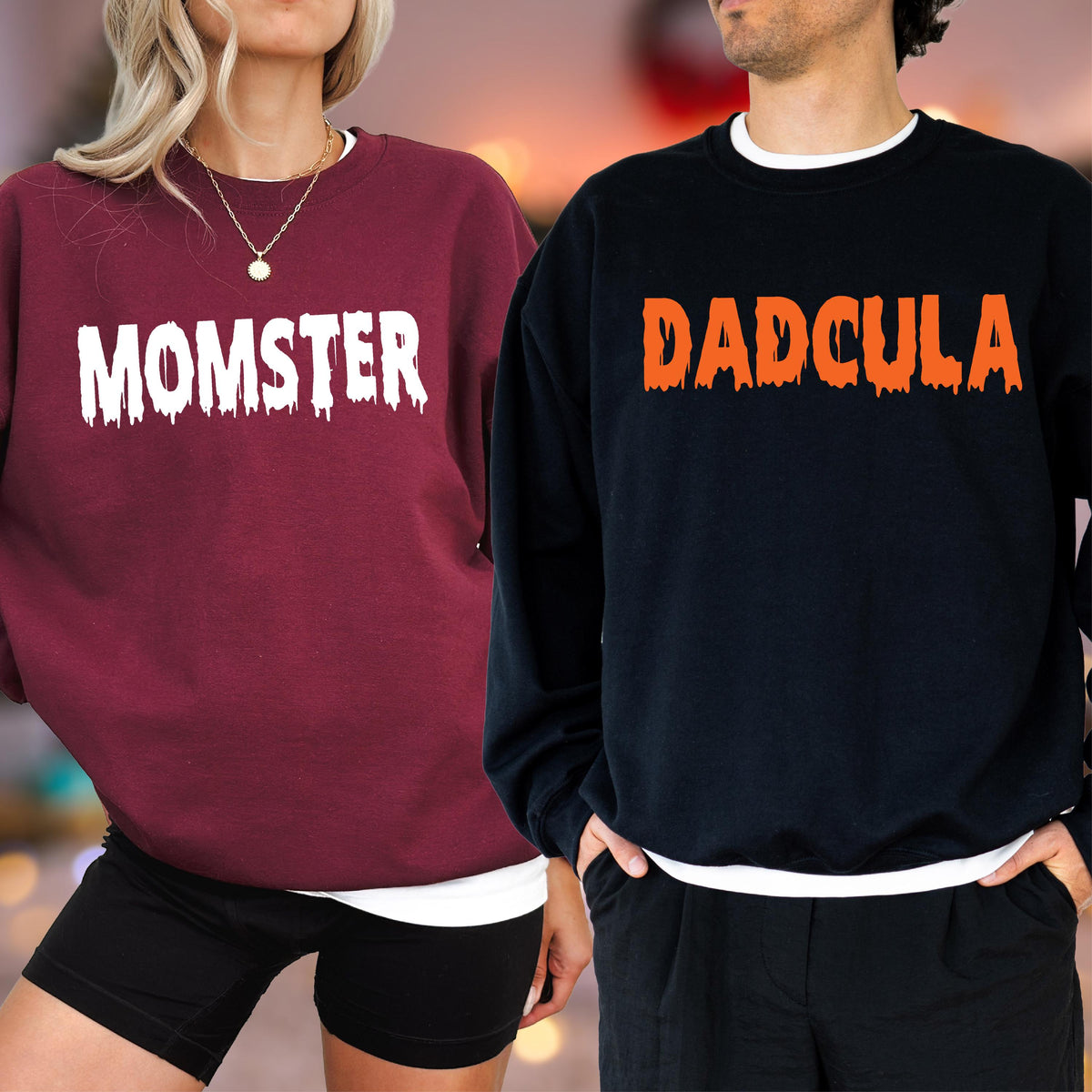 May include: Two sweatshirts, one burgundy and one navy blue. The burgundy sweatshirt has the word "MOMSTER" in white dripping font. The navy blue sweatshirt has the word "DADCULA" in orange dripping font. Both sweatshirts have a white crew neck.