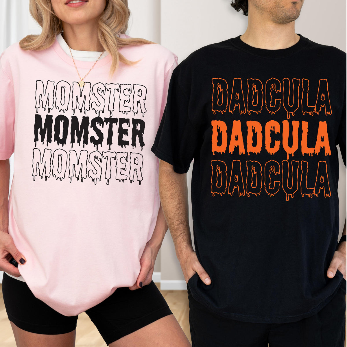 May include: Two t-shirts, one pink and one black, with Halloween-themed text. The pink shirt says "MOMSTER" in dripping black letters. The black shirt says "DADCULA" in dripping orange letters. Both shirts are short-sleeved.