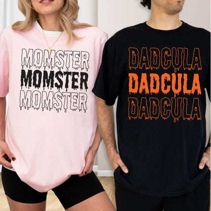 May include: Two t-shirts, one pink and one black, with Halloween-themed text. The pink shirt says "MOMSTER" in dripping black letters. The black shirt says "DADCULA" in dripping orange letters. Both shirts are short-sleeved.
