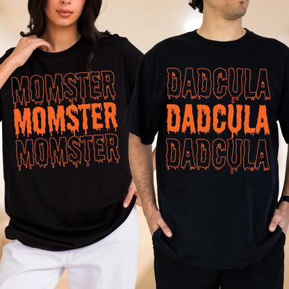 May include: Black t-shirts with orange text. One shirt says "MOMSTER" three times, and the other says "DADcula" three times. The text has a dripping effect, creating a spooky Halloween theme.