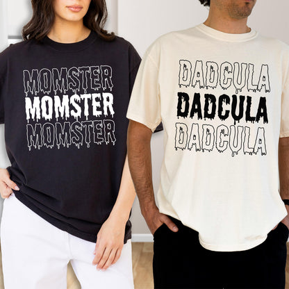 May include: Two t-shirts, one black and one cream, each with a unique graphic. The black shirt features the word "MOMSTER" three times in white, with a dripping effect. The cream shirt displays "DADcula" three times in black.