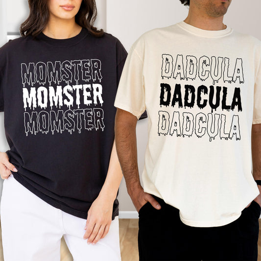 May include: Two t-shirts, one black and one cream, each with a unique graphic. The black shirt features the word "MOMSTER" three times in white, with a dripping effect. The cream shirt displays "DADcula" three times in black.