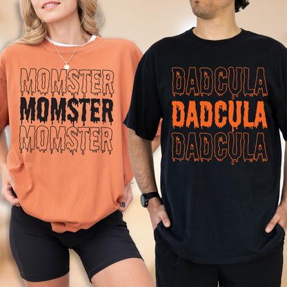 May include: Two t-shirts, one orange and one black, with Halloween-themed text. The orange shirt says "MOMSTER" three times in black dripping font. The black shirt says "DADcula" three times in orange dripping font. Both shirts are short-sleeved.