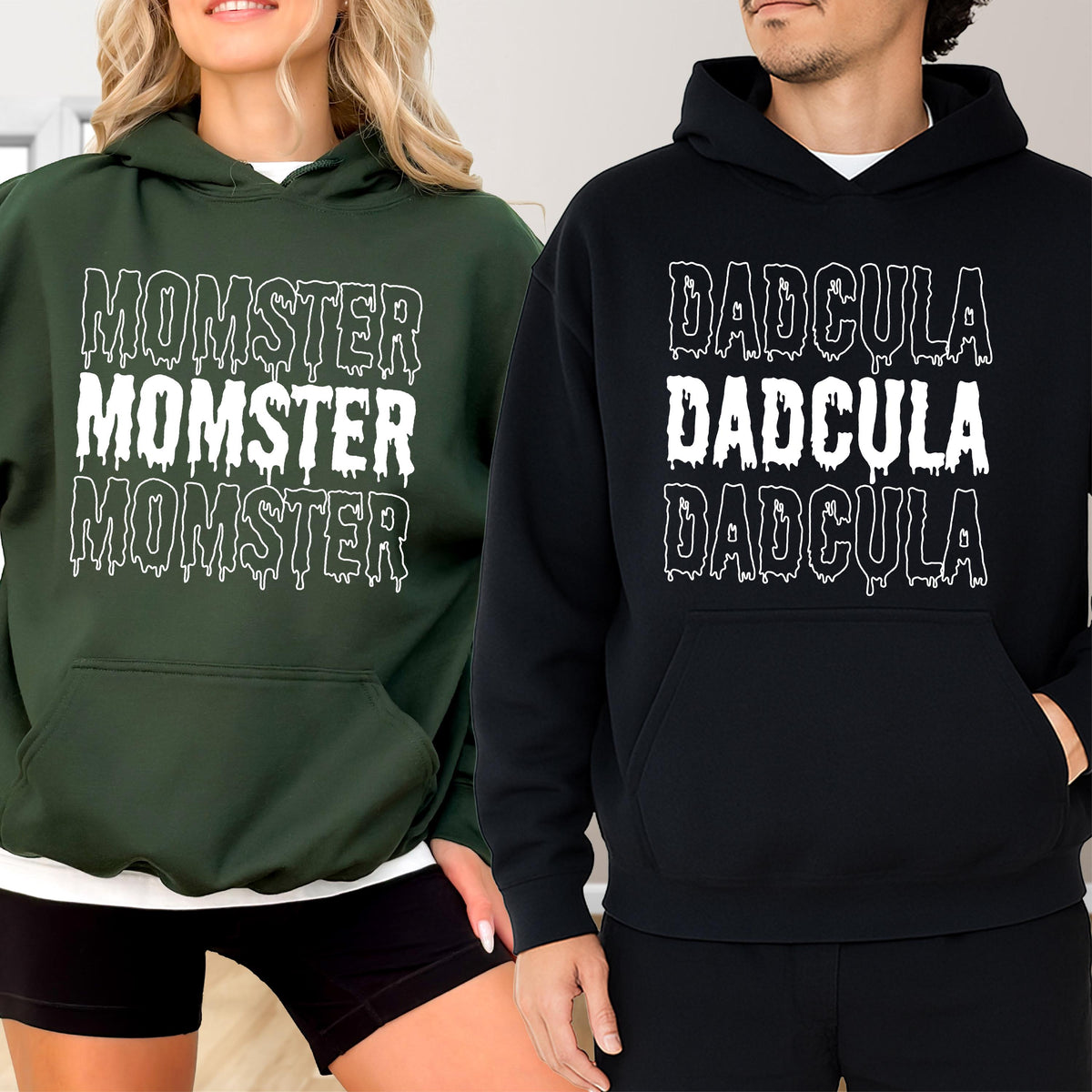 May include: Two hooded sweatshirts, one dark green and one black. The dark green sweatshirt has the word "MOMSTER" printed three times in white, with a dripping effect. The black sweatshirt has the word "DADCULA" printed three times in white, with a dripping effect.