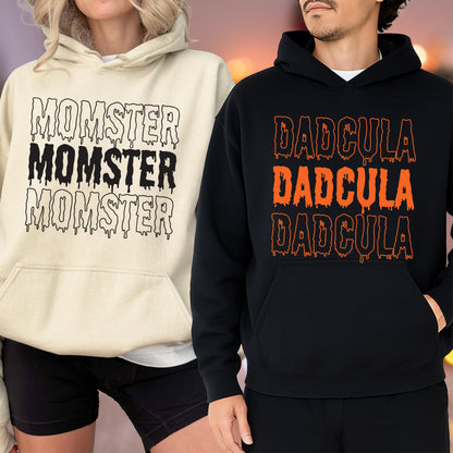 May include: Two hooded sweatshirts, one cream-colored and one black. The cream sweatshirt has the word "MOMSTER" printed three times in a dripping font. The black sweatshirt has the word "DADCULA" printed three times in an orange dripping font.