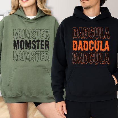 May include: Two hooded sweatshirts, one olive green and one black. The olive green sweatshirt has the word "MOMSTER" printed three times in black. The black sweatshirt has the word "DADcula" printed three times in orange.