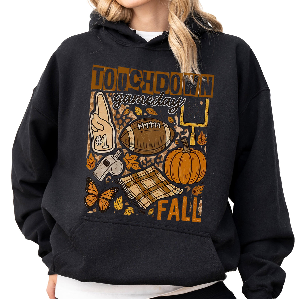 May include: Black hoodie with a fall-themed graphic. The design includes a football, pumpkin, leaves, and the words "TOUCHDOWN gameday FALL". A foam finger, whistle, and butterfly are also featured.