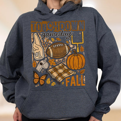 May include: Dark gray hoodie with a football-themed graphic. The design includes a football, pumpkin, and the words "Touchdown Gameday Fall". Other elements include a foam finger, whistle, butterfly, and a plaid blanket.