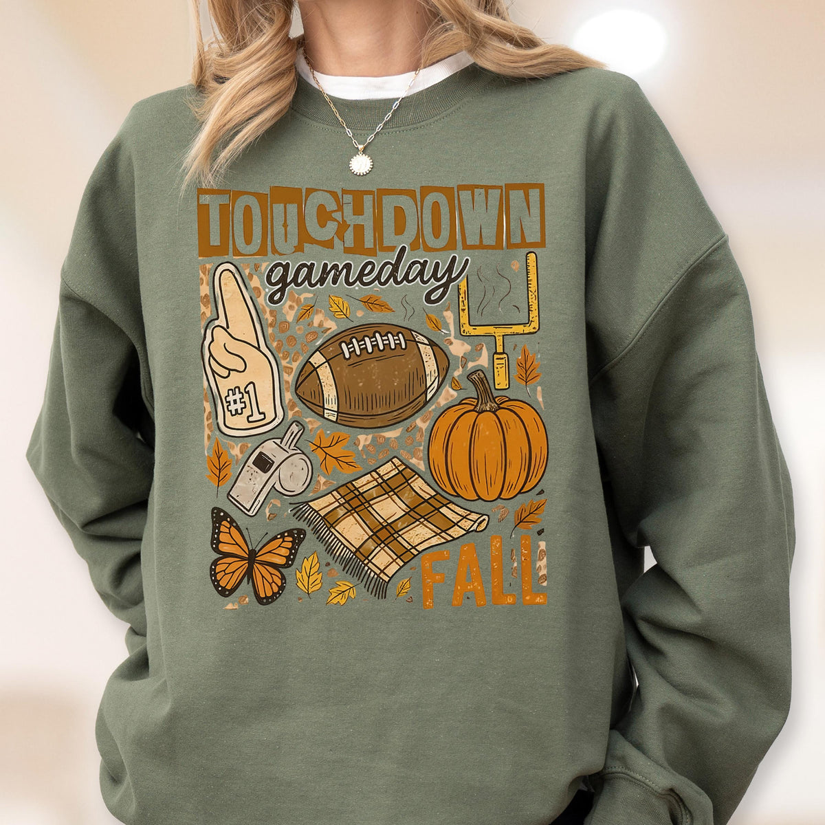May include: Green sweatshirt with a graphic design featuring the words "TOUCHDOWN gameday FALL". The design includes a football, pumpkin, foam finger, whistle, butterfly, and a plaid blanket.