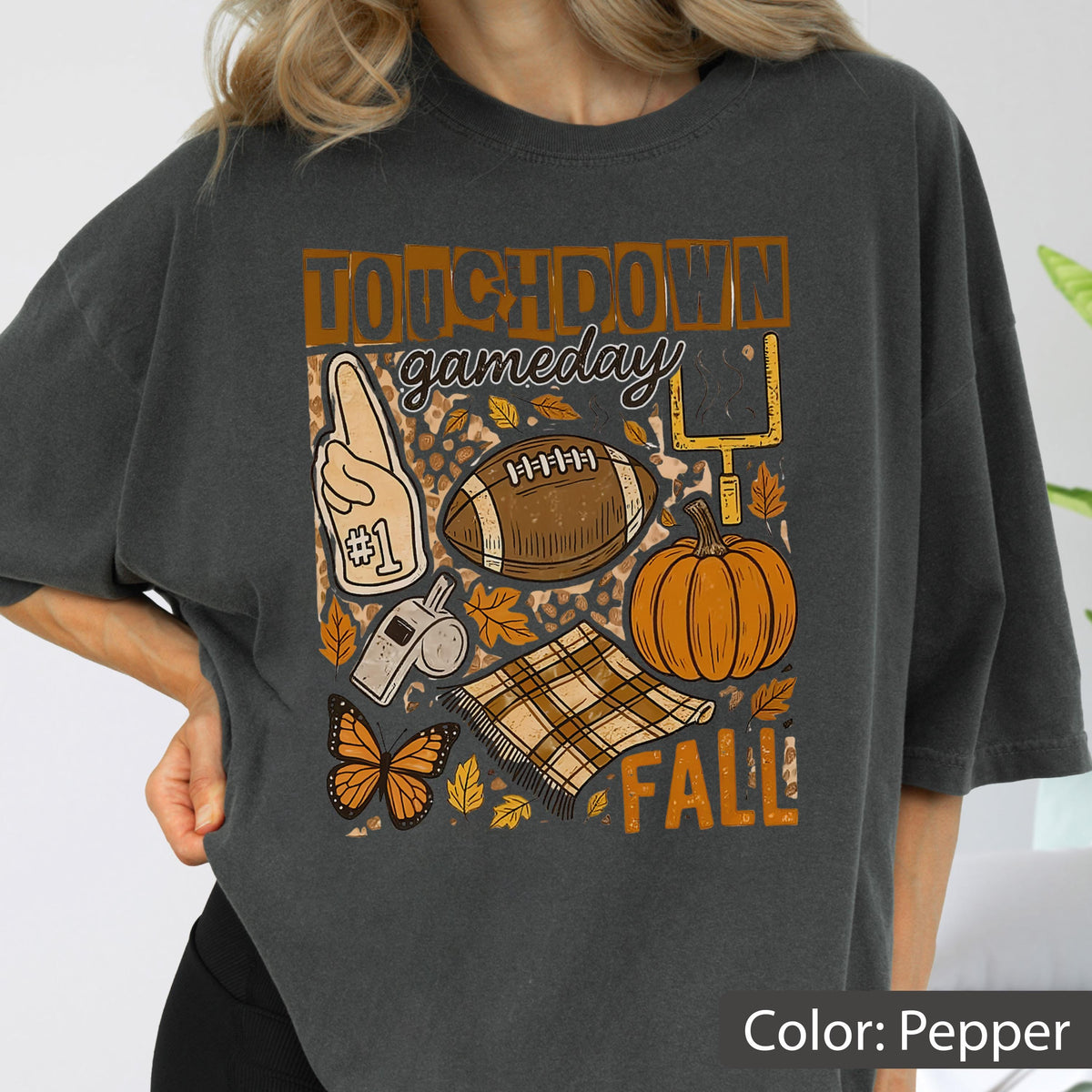 May include: Pepper-colored t-shirt with a fall-themed graphic. The design includes a football, pumpkin, and the words "Touchdown Gameday Fall." Other elements include a foam finger, a whistle, a butterfly, and a plaid blanket.