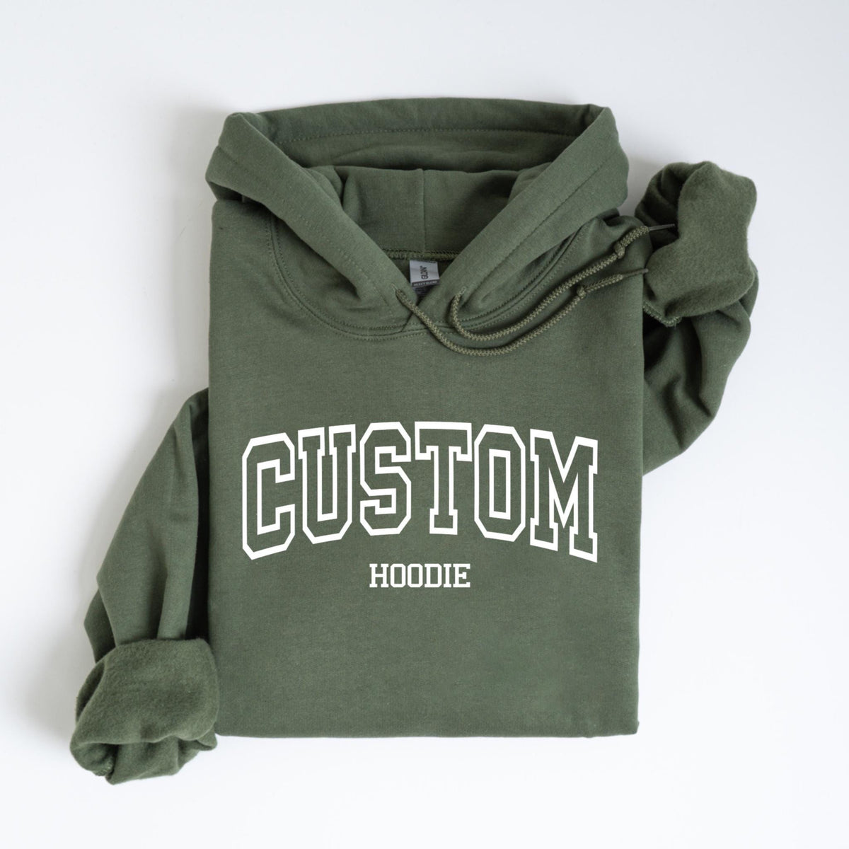May include: An olive green hoodie with white text that reads "CUSTOM HOODIE" in a collegiate font. The hoodie has a drawstring hood and long sleeves. The garment is folded neatly on a white surface.