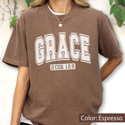 May include: An espresso brown short-sleeve t-shirt featuring the word GRACE in large, white, collegiate-style block lettering across the chest, with the text 2 COR 12:9 printed in a smaller white font directly underneath the main word.