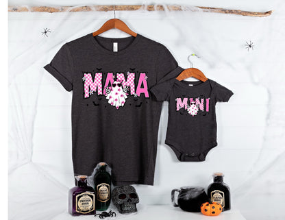 May include: A dark gray t-shirt and a matching dark gray baby bodysuit. Both garments feature a pink and white checkered graphic with the text MAMA on the shirt and MINI on the bodysuit, each accompanied by a ghost wearing sunglasses and making a peace sign.